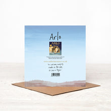 Load image into Gallery viewer, Back of blue square happy birthday card, featuring lion illustration of Arlo, standing on matching brown envelope.