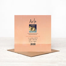 Load image into Gallery viewer, A pink square greetings card stood on its matching brown envelope, showing the back details of the card, including a picture of the book Arlo The Lion Who Couldn&#39;t Sleep, by Catherine Rayner, the barcode and website. 