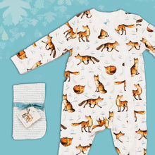 Load image into Gallery viewer, Baby gift set comprising a white babygrow featuring an illustrated fox print and matching dribble cloths tied in turquoise ribbon, on a blue backdrop with decorated leaves. 