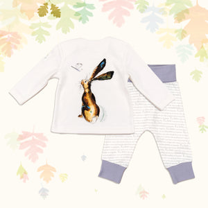 Baby gift set comprising a white top featuring a front and back illustrated hare print and matching bottoms with purple cuffs, on a backdrop of pastel leaves.