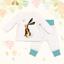 Load image into Gallery viewer, Baby gift set comprising a white top showing the reverse of an illustrated hare print and matching bottoms with ocean blue cuffs, on a backdrop of illustrated pastel leaves. 