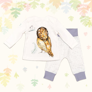 Baby gift set comprising a white long-sleeved top showing back of an illustrated owl print and matching bottoms with purple cuffs, on a backdrop of pastel leaves. 