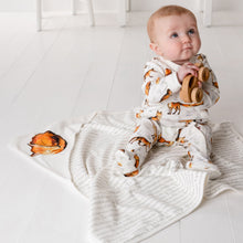 Load image into Gallery viewer, One year-old baby wearing the dexter babygrow sitting on the matching dexter fox hooded blanket. The babygrow is white and features a repeat print of Dexter Fox while the blanket features a story print and a fox print on the hood. 