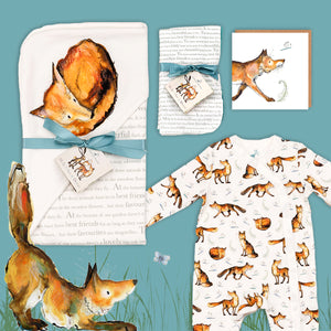 Dexter fox themed baby gift hamper containing a fox print hooded blanket, a fox babygrow, a matching fox card and dribble cloths. They are laid out on a blue background with illustrated Dexter fox stretching below. 