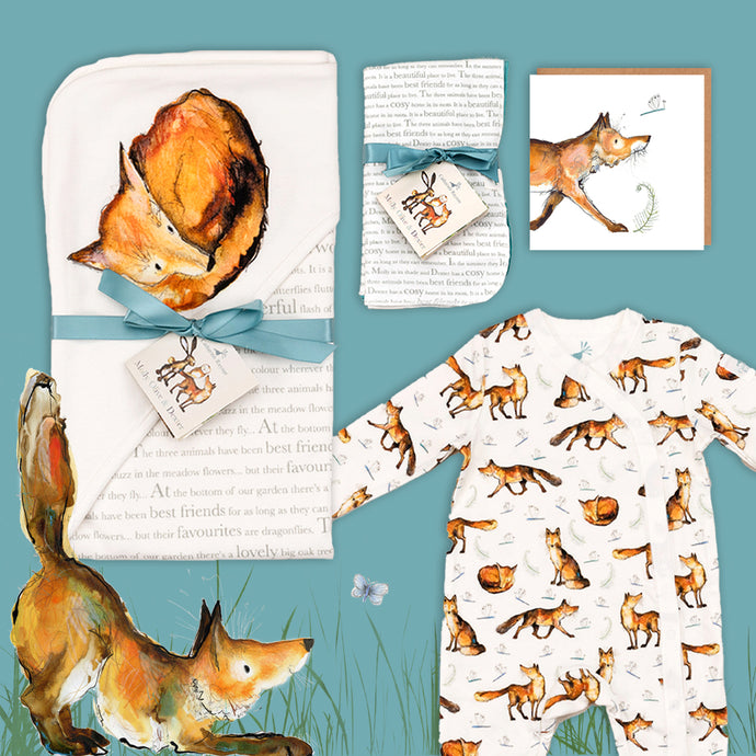 Dexter fox themed baby gift hamper containing a fox print hooded blanket, a fox babygrow, a matching fox card and dribble cloths. They are laid out on a blue background with illustrated Dexter fox stretching below. 