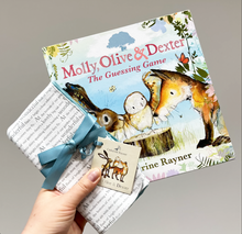 Load image into Gallery viewer, Hand holding out storytime dribble cloths tied in turquoise ribbon and matching book, Catherine Rayner&#39;s &#39;Molly, Olive and Dexter: The Guessing Game.&#39;