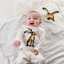 Load image into Gallery viewer, Baby wearing Molly hare long sleeved top and matching joggers lying on their back smiling on top of Molly hare hooded blanket. The blanket and joggers feature the same exclusive story print by Catherine Rayner.