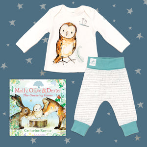 Baby gift set featuring a book from the Molly, Olive and Dexter series by Catherine Rayner, 'The Guessing Game', and a matching owl pyjama set laid on a midnight blue backdrop with silver stars. The pyjama set comprises a white long-sleeved top featuring an illustrated wraparound owl print and matching bottoms with blue cuffs.