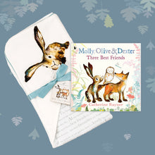 Load image into Gallery viewer, Baby gift set featuring a book from the Molly, Olive and Dexter series by Catherine Rayner, &#39;Three Best Friends&#39;, and a matching hare blanket laid on a dusty blue backdrop with pastel leaves. The blanket has a hood featuring Molly Hare and is wrapped with a turquoise ribbon. 