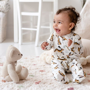 One year-old baby girl sat up laughing wearing Molly Hare repeat print babygrow. 