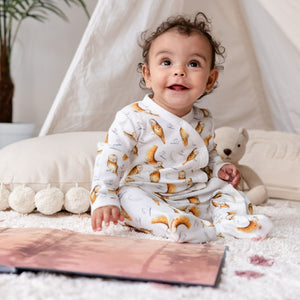 6 month old baby sat looking up in front of a book, wearing the illustrated olive owl babygrow. 