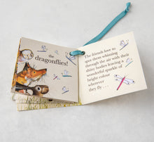 Load image into Gallery viewer, Close-up image of the mini story booklet that comes attached to every babywear item with turquoise ribbon. The pages show Molly Hare, Dexter Fox and Olive Owl spotting pink, blue and purple dragonflies in the air. 