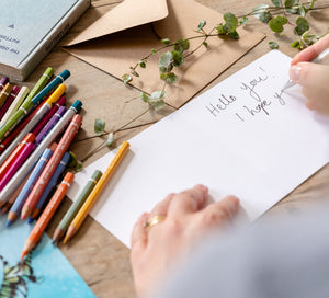 Catherine handwriting a personalised message in a greetings card, surrounded by art supplies.