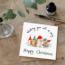 Load image into Gallery viewer, Christmas card featuring illustration of guinea pigs wearing red and green  christmas hats laid flat on a wooden table with a matching brown envelope. 