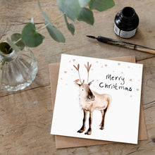 Load image into Gallery viewer, Christmas card featuring illustration of Adolphus Reindeer laid flat on a wooden table with a matching brown envelope. 