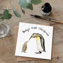 Load image into Gallery viewer, Christmas card laid flat on a wooden table  featuring an illustration of. mum and baby penguin with message that reads &#39;Baby&#39;s First Christmas&#39;