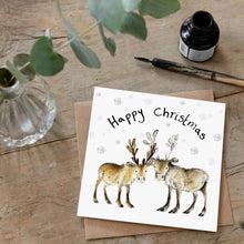 Load image into Gallery viewer, Christmas card with an illustration of Baby reindeers Miriam and Madeleine and handwritten &#39;Happy Christmas&#39; message, laid flat on a wooden table alongside matching brown envelope. 