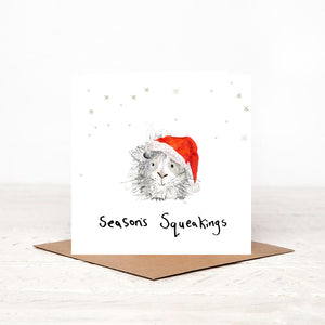 Square illustrated guinea pig Christmas card stood on matching brown craft envelope. 