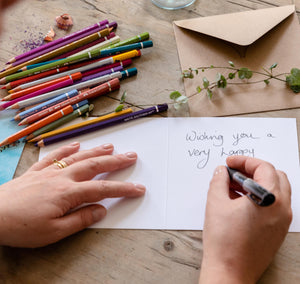 Christmas card being personalised with a handwritten message on a wooden desk