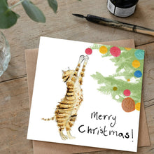 Load image into Gallery viewer, Christmas card featuring illustration of Posy Kitten laid flat on a wooden table on top of a matching brown envelope.